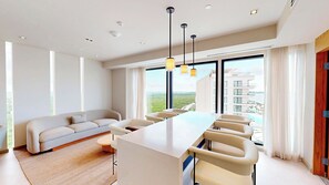 A modern hotel room with a large window, a sofa, a dining table with chairs, and pendant lighting.