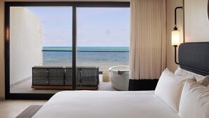A hotel room with a large bed, a view of the ocean, a seating area with a cushioned bench, and a wall-mounted light fixture. - AVA Resort Cancun (Cancun)
