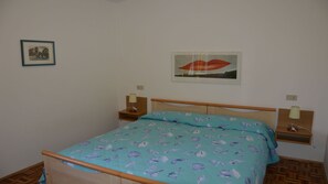 A bedroom with a bed, two bedside tables, a nightstand, a wall-mounted lamp, and a framed picture. - Bright villa in Caorle with private garden (Caorle)