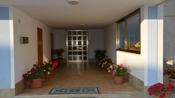 A hallway with a tiled floor, a door at the end, and potted plants on either side.