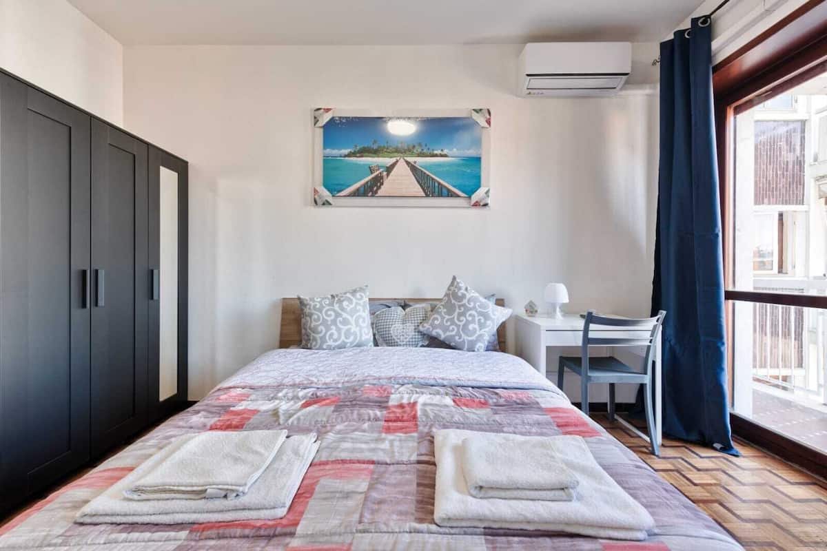 Ein Schlafzimmer mit Bett, Schreibtisch, Stuhl, Kleiderschrank und einem Bild von einem Pier.