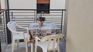 Een klein balkon buiten met een tafel bezaaid met kranten, twee witte plastic stoelen en een potplant.