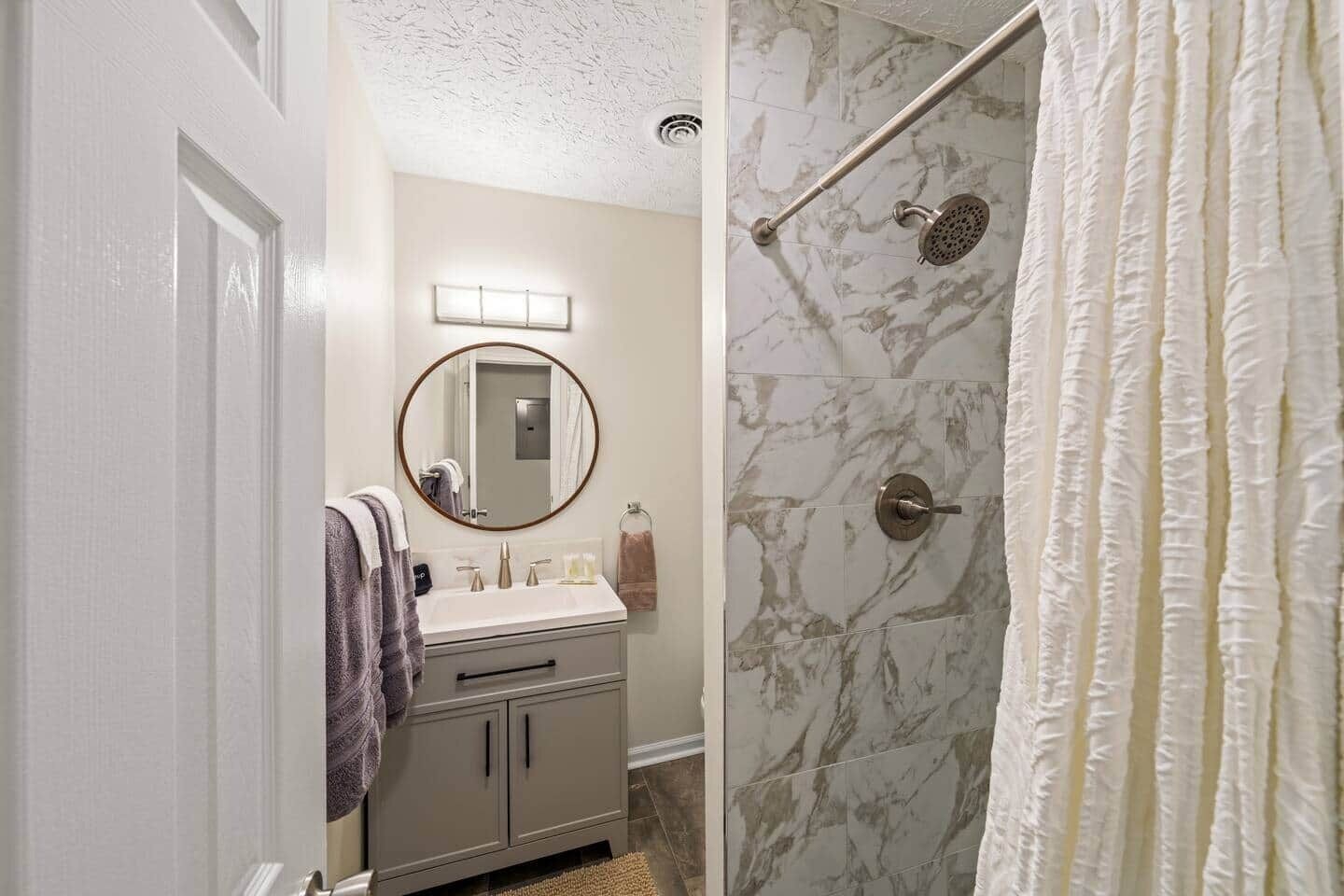 A bathroom with a shower, a sink with a mirror, and a towel rack.