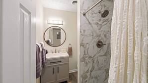 A bathroom with a shower, a sink with a mirror, and a towel rack.