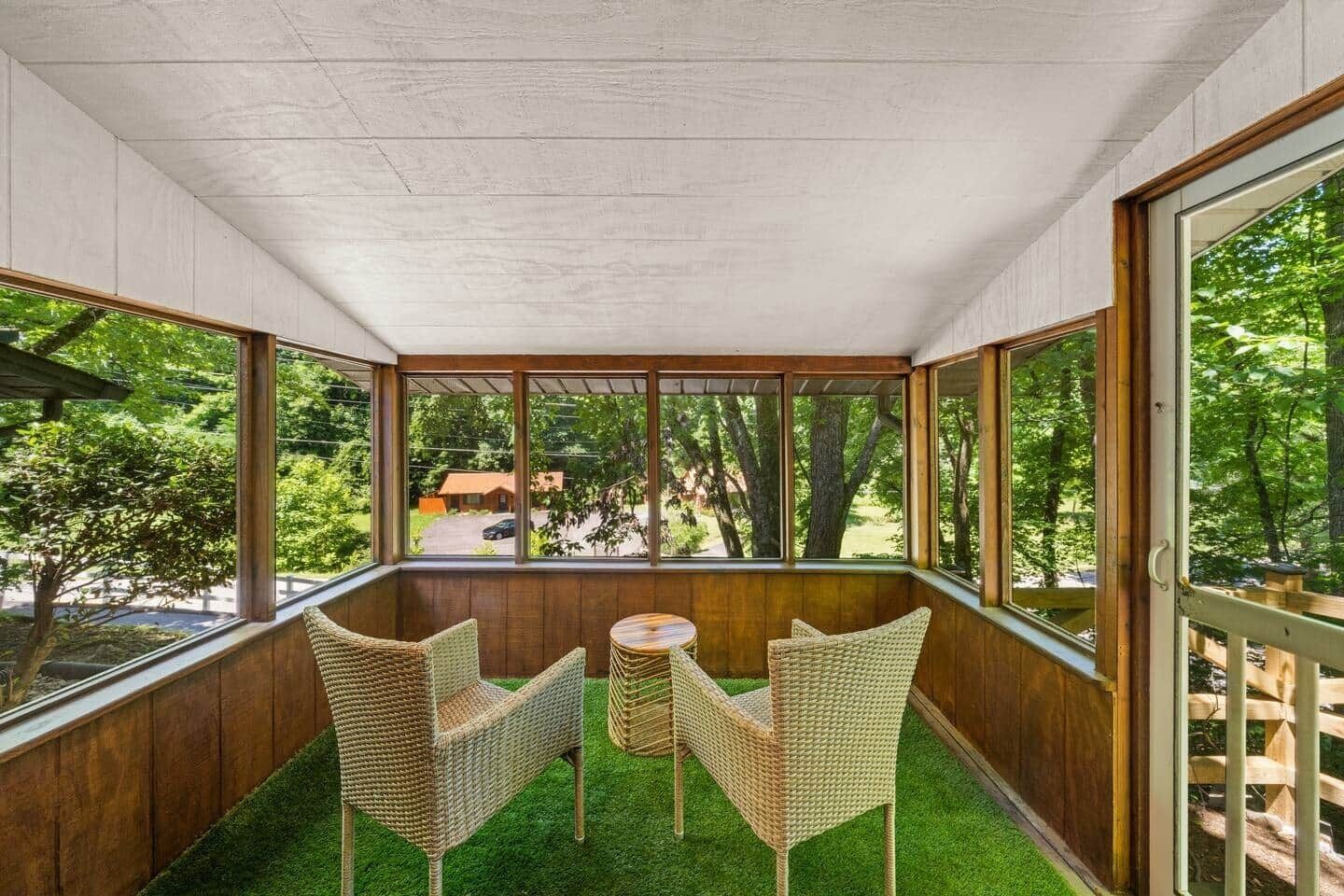 Une terrasse couverte, aménagée avec des meubles en osier et une petite table, d’où l’on peut admirer un paysage verdoyant et un bâtiment situé au loin.