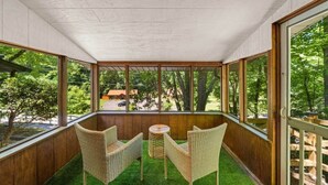 A covered patio with wicker furniture and a small table, overlooking a green landscape and a distant building.