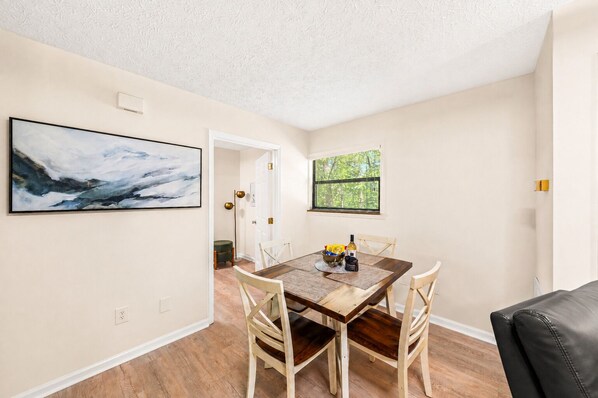 A dining area with a wooden table, white chairs, and a painting on the wall.