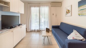 Una sala de estar moderna con un televisor de pantalla plana, un sofá, una mesa de centro y un comedor con una mesa y sillas.