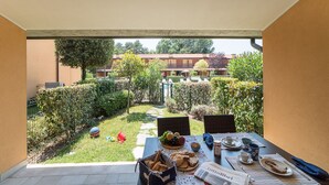Un patio con mesa lista para el desayuno, vistas a un jardín y un edificio al fondo.