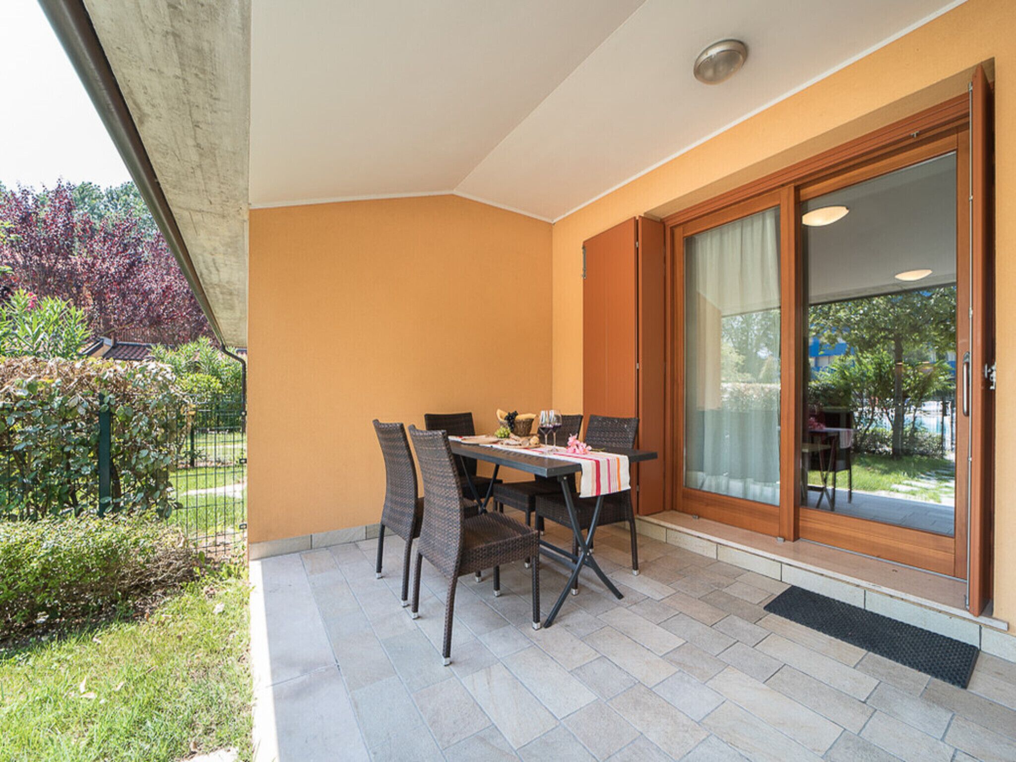 Een overdekt terras met een tafel en stoelen, een schuifpui en uitzicht op een tuin.