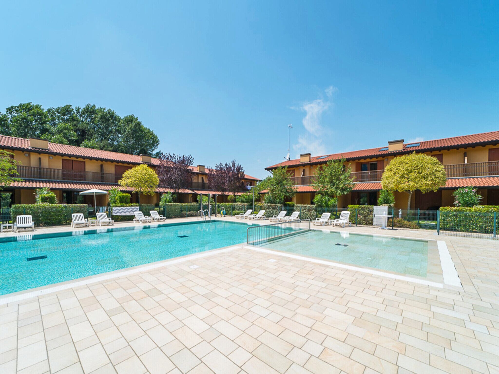 A pool area with tiled flooring, lounge chairs, and a clear blue sky.