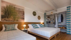 A bedroom with two beds, wooden headboard, a nightstand with a lamp, a wall-mounted shelf with clothes, and a large painting of a beach scene.