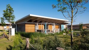A modern building with a flat roof and wooden siding, surrounded by greenery and a clear sky.