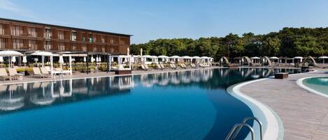A swimming pool with lounge chairs and umbrellas, a wooden building, and a forested area in the background.