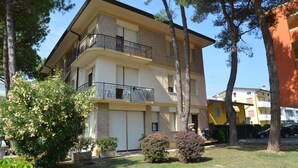 A multi-story residential building with balconies, surrounded by trees and a well-maintained lawn. - Family house with beautiful terrace (Bibione)