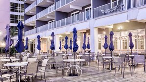 An outdoor dining area with tables and chairs, umbrellas, and a wooden deck. - PCB SNOWBIRDS PARADISE/GOLF/5POOLS/SOME HEATED/STEPS TO BEACH (Panama City Beach)