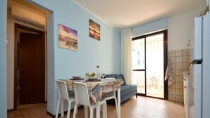 A dining area with a table set for four, a sofa, and a kitchen area with a refrigerator. - Comfortable holiday home near the sea (Bibione)