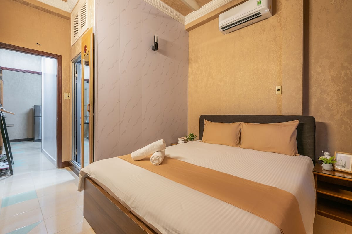 A hotel room with a neatly made bed, a bedside table with a lamp, and a door leading to a bathroom.