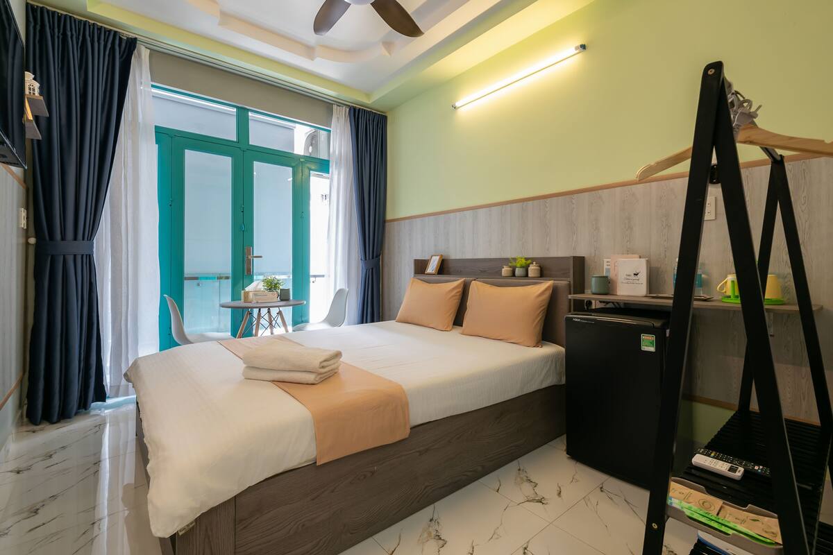 A hotel room with a bed, a desk, a chair, a small table, and a wardrobe.