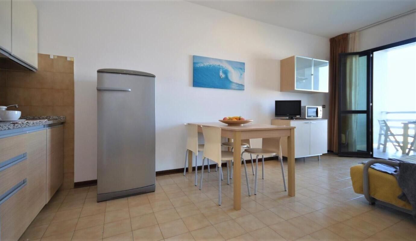 Una cocina compacta con refrigerador, una mesa de comedor con sillas, microondas y televisor.