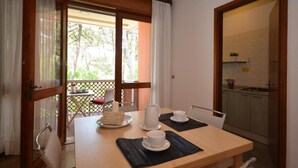 A dining area with a table set for two, a kitchen visible through an open door, and a view of a balcony with outdoor furniture.
