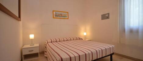 A bedroom with a bed, two bedside lamps, a nightstand, a framed picture on the wall, and a window with curtains.