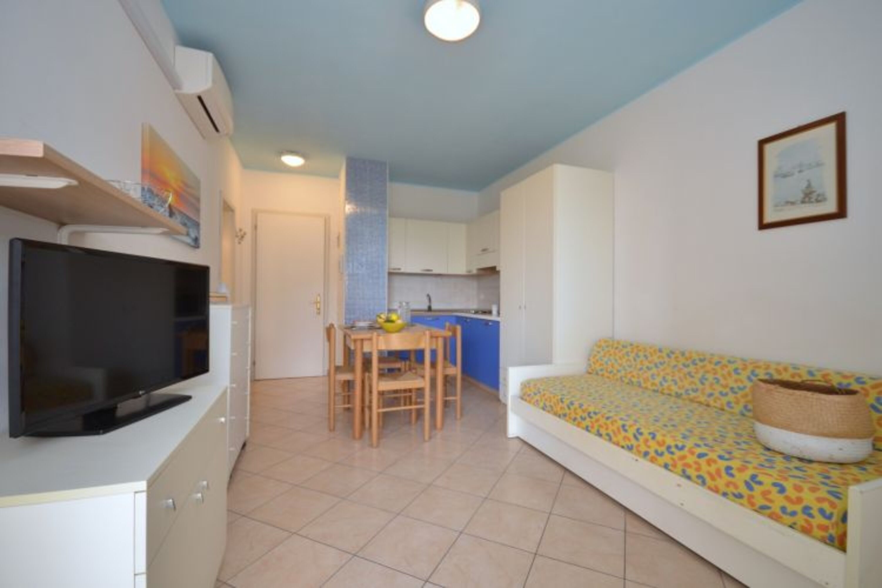 Un espacio habitable compacto con televisor, kitchenette, comedor y sofá.