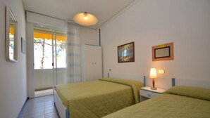 Ein Zimmer mit zwei Betten, einem Fenster mit Vorhängen, einem Nachttisch mit Lampe und einem Gemälde an der Wand.