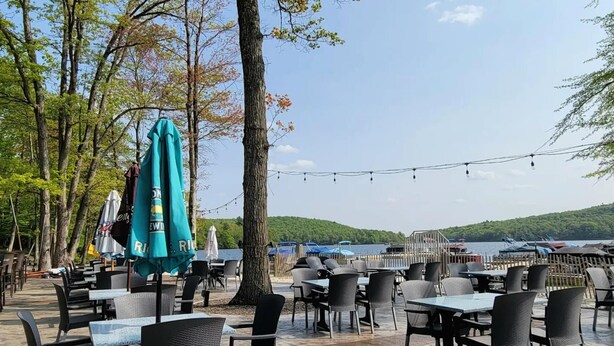 An outdoor dining area with tables and chairs, umbrellas, and a view of the water and hills. - Pocono Retreat -1 Mile to Lake and Skiing (Lake Harmony)