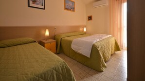 A hotel room with two single beds, a nightstand with a lamp, a wall-mounted air conditioner, and two framed pictures. - Spacious and bright apartment (Bibione)
