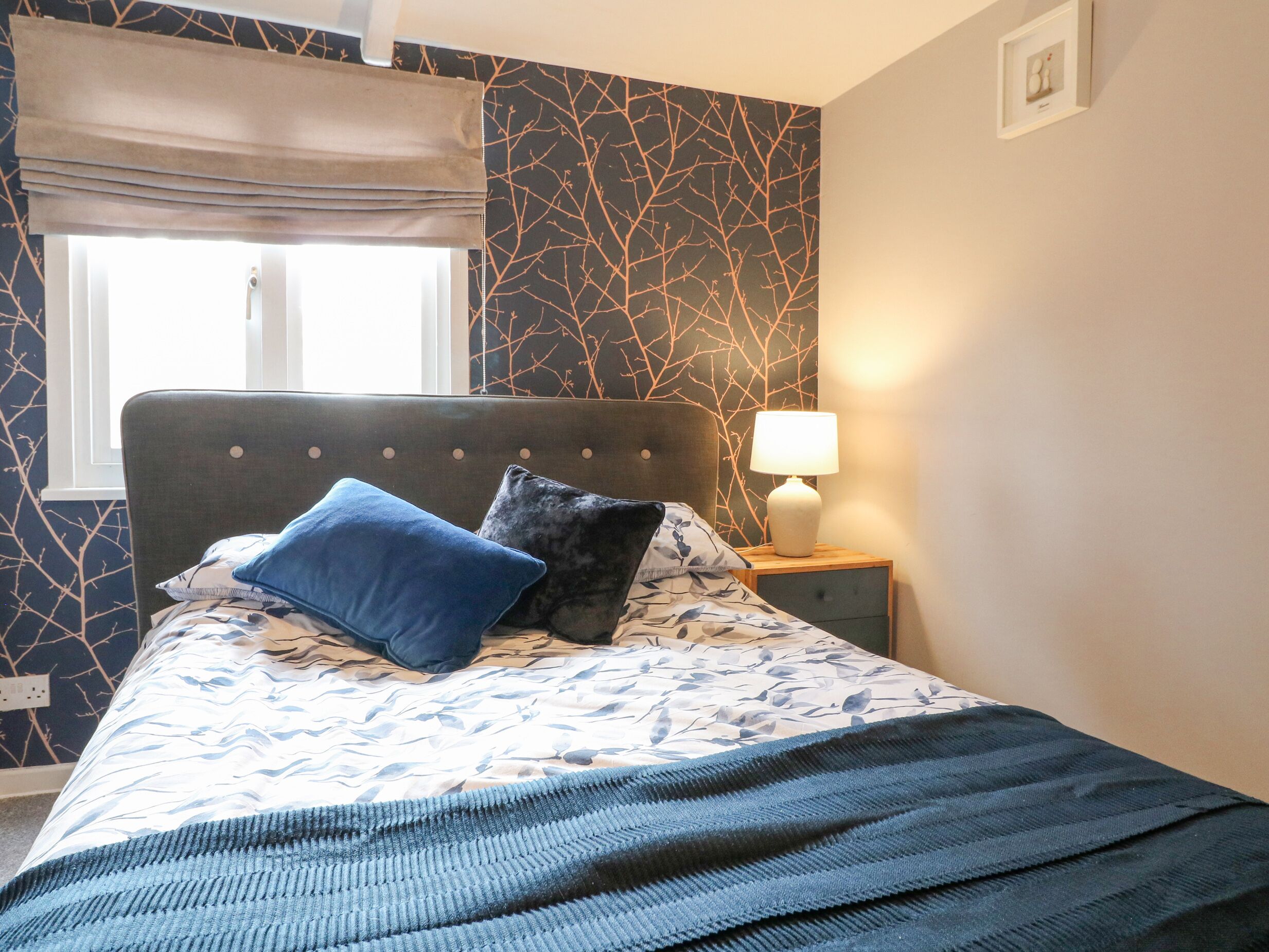 A bedroom with a bed, a nightstand, a lamp, and a window with a curtain.