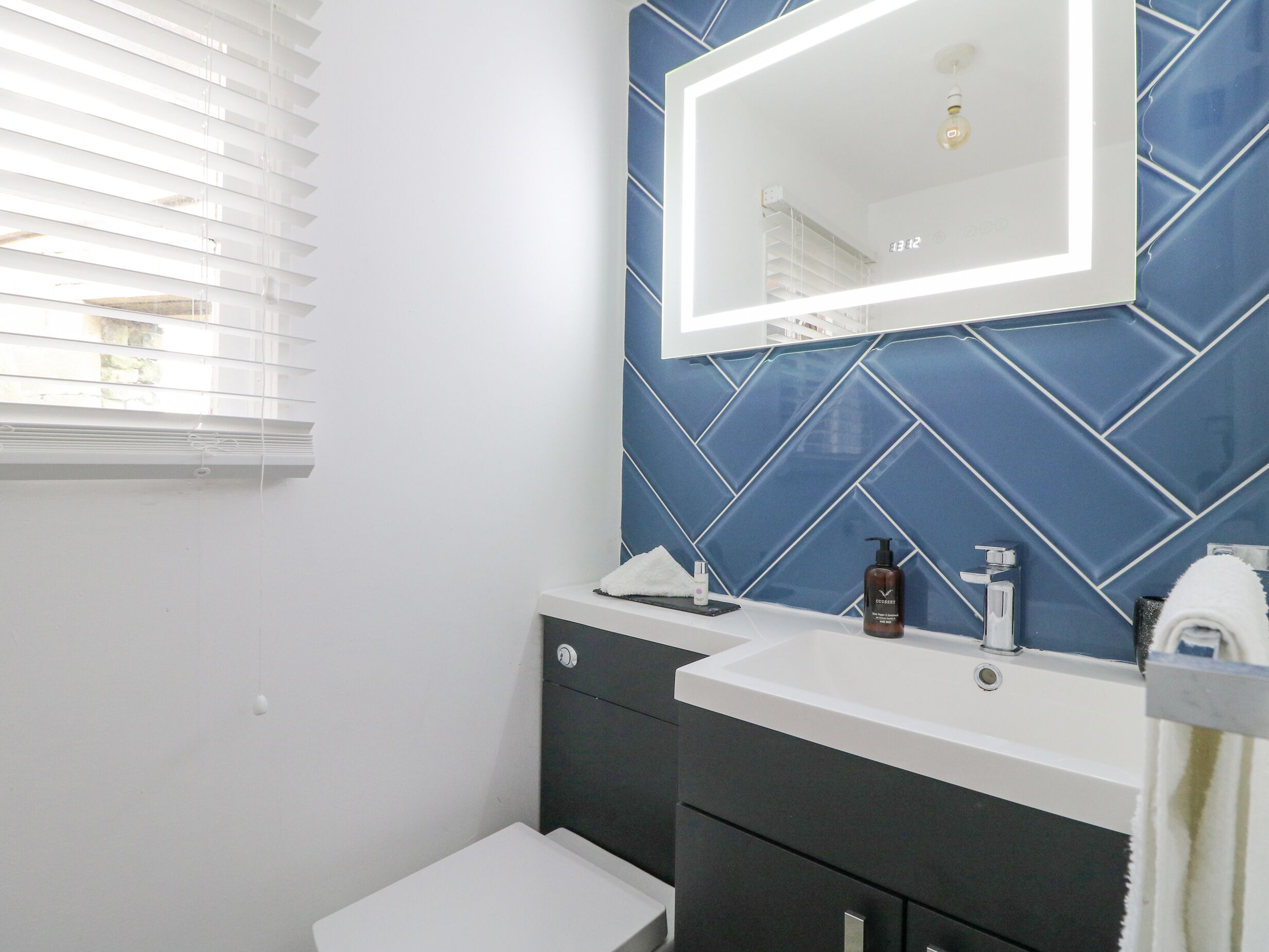 A bathroom with a white sink, dark vanity, and a mirror with a lighted frame.
