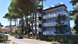 Un immeuble à plusieurs étages doté de balcons, entouré d’arbres et avec une voiture garée à proximité.