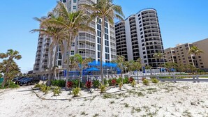 A beachfront hotel with multiple high-rise buildings, palm trees, and a sandy beach area. - Gullwing Resort 1002- A beachfront condo with amazing beach and bay views (Fort MyersBeach)
