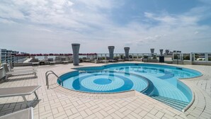 Piscina no terraço com design circular, espreguiçadeiras e céu claro.