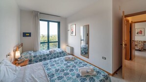 Quarto de hotel com duas camas, uma janela grande, um espelho e uma porta para uma varanda.