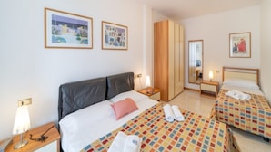 Habitación de hotel con una cama grande, dos camas más pequeñas, un armario y dos cuadros en la pared.