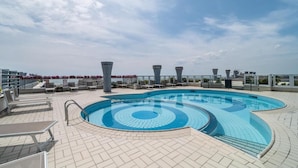 Una piscina en la azotea con diseño circular, sillas de descanso y cielo despejado.