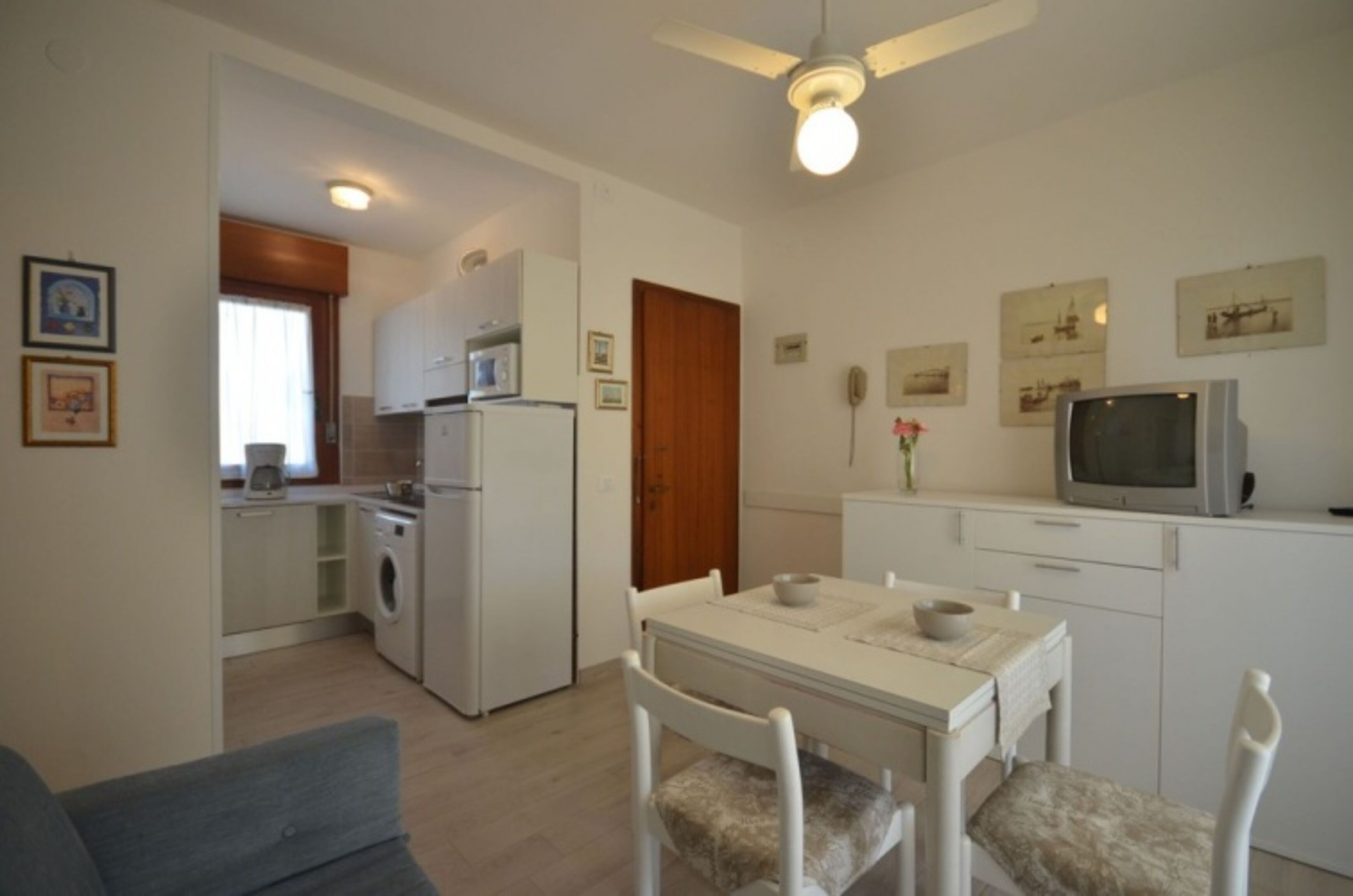 A compact kitchen with a microwave, refrigerator, and washing machine. There is a dining area with a table and chairs.