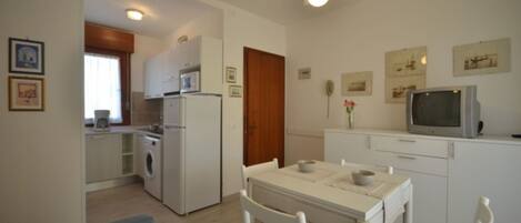 A compact kitchen with a microwave, refrigerator, and washing machine. There is a dining area with a table and chairs.