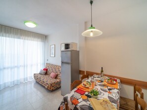 En moderne stue med sofa, spisebord dækket til et måltid og et køleskab.