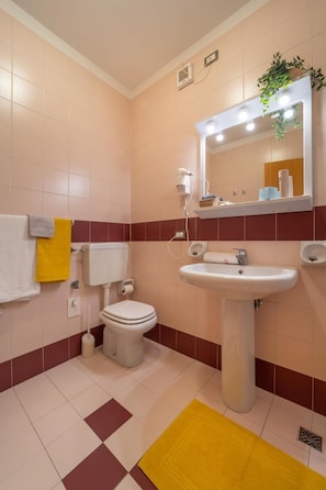 Ein Badezimmer mit Toilette, Waschbecken und Spiegel. Auf dem Boden liegt ein gelber Teppich.