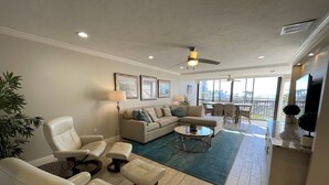 A spacious living room with a large sofa, two armchairs, a coffee table, and a dining area with a view of the outdoors. - Exquisite Deluxe beachfront condo (Sarasota)
