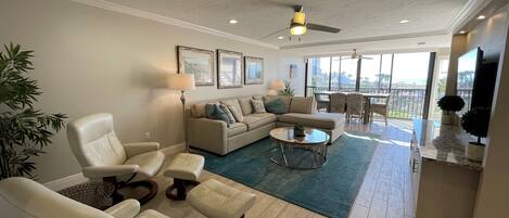 A spacious living room with a large sofa, two armchairs, a coffee table, and a dining area with a view of the outdoors.