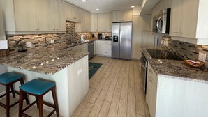 A modern kitchen with granite countertops, stainless steel appliances, and light wood cabinetry. - Exquisite Deluxe beachfront condo (Sarasota)
