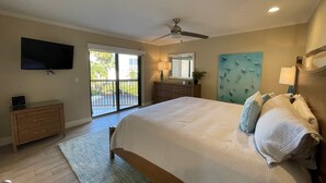 A bedroom with a large bed, a ceiling fan, a TV, a dresser, and a view of the outdoors. - Exquisite Deluxe beachfront condo (Sarasota)
