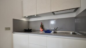 Cozinha moderna com armários brancos, pia de aço inoxidável e forno embutido.