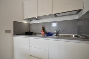 A modern kitchen with white cabinets, a stainless steel sink, and a built-in oven. - Functional seaside house with pool (Bibione)