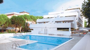 Piscina com deck ladrilhado, cercada por edifícios e árvores.
