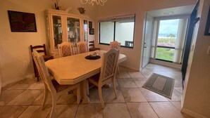 A dining area with a large table, chairs, a chandelier, and a view of the outdoors through a glass door. - Cresent Beach Gulf view 2Bd/2Ba Condo (Sarasota)